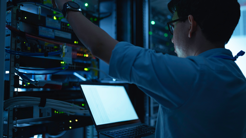 Man with laptop working in a server room.
